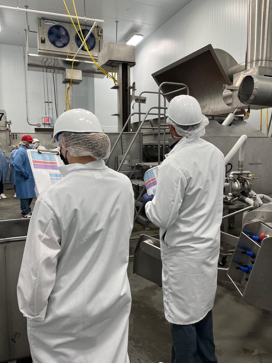 Two developers in lab coats and hard hats reviewing trial sheets on the factory floor
